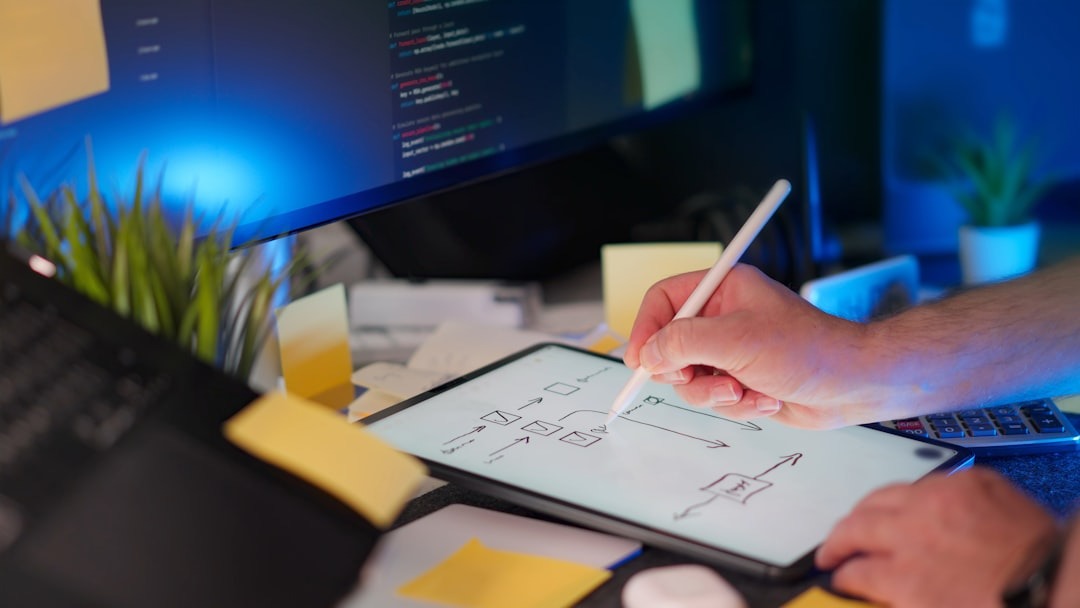 Hand using stylus to draw flowchart on tablet with computer monitor.